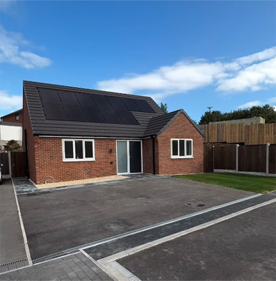 Single-storey red-brick home with a dark pitched roof, solar panels, driveway, small lawn and fenced garden.